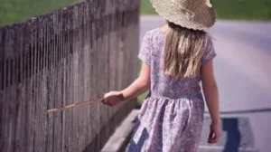 niña paseando en calle con palo tocando valla en representación despertar espiritual volver a ti mismo
